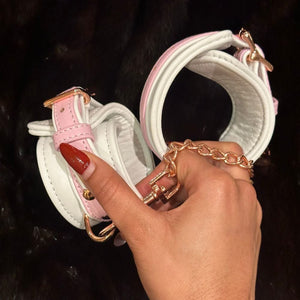 Image des Menottes en Cuir Couleur Blanc et Rose portées sur fond de Fourrure Noir