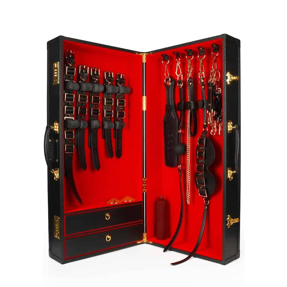 Coffret BDSM ouvert en cuir noir avec intérieur rouge, présentant un ensemble d’accessoires assortis comprenant menottes, sangles, cravaches et chaînes, disposés de manière ordonnée dans une esthétique luxueuse.