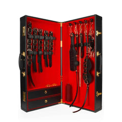 Coffret BDSM ouvert en cuir noir avec intérieur rouge, présentant un ensemble d’accessoires assortis comprenant menottes, sangles, cravaches et chaînes, disposés de manière ordonnée dans une esthétique luxueuse.
