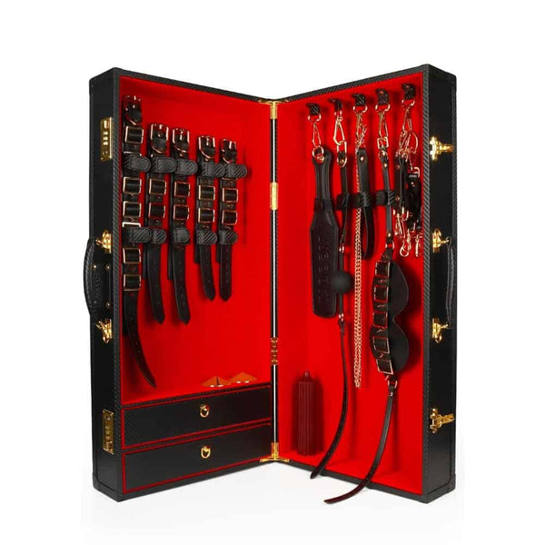 Coffret BDSM ouvert en cuir noir avec intérieur rouge, présentant un ensemble d’accessoires assortis comprenant menottes, sangles, cravaches et chaînes, disposés de manière ordonnée dans une esthétique luxueuse.
