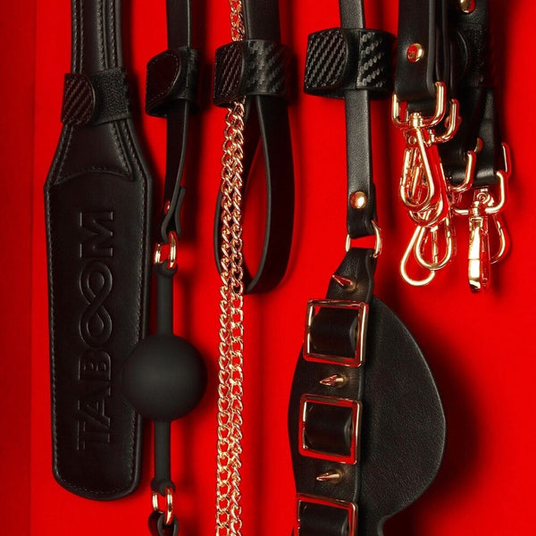 Coffret BDSM ouvert en cuir noir avec intérieur rouge, présentant un ensemble d’accessoires assortis comprenant menottes, sangles, cravaches et chaînes, disposés de manière ordonnée dans une esthétique luxueuse.