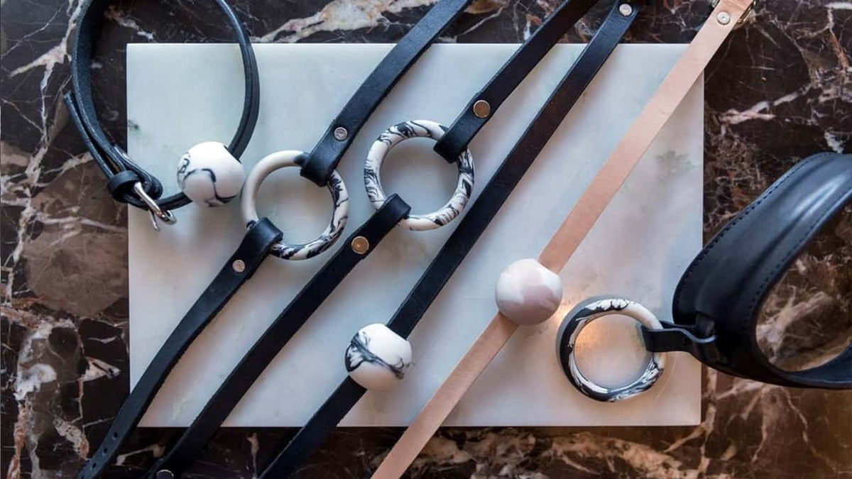 Collier en cuir de couleur noir et beige, bande fine et un collier épais. sur chaque collier se trouve un anneau ou une boule avec un motif marbre.