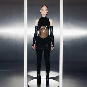 Combinaison en latex noir ANOESES avec empiècement transparent au buste, manches longues et col montant, portée par un modèle debout dans un décor minimaliste.