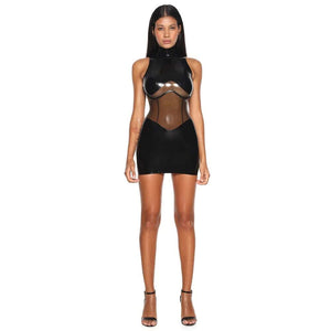 Body en latex noir ANOESES avec col montant et empiècements transparents, porté par un mannequin assis sur un fauteuil en cuir noir, vue légèrement plongeante.