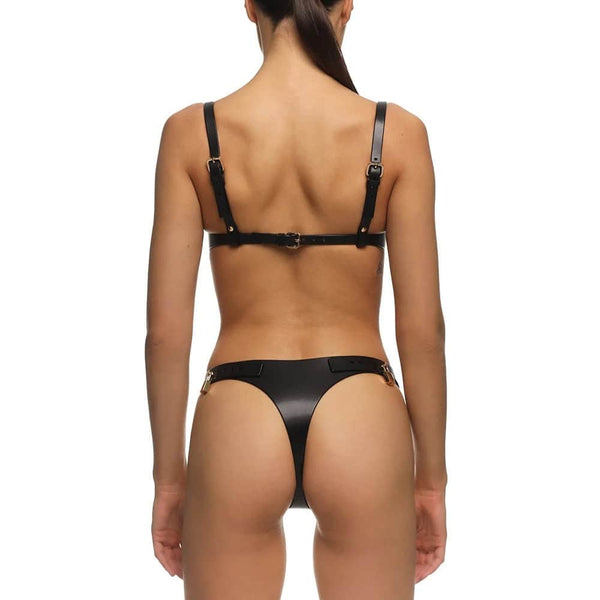 Soutien-gorge ANOESIS en cuir noir avec armatures, sangles réglables et finitions métalliques dorées, porté avec un string assorti sur fond blanc.