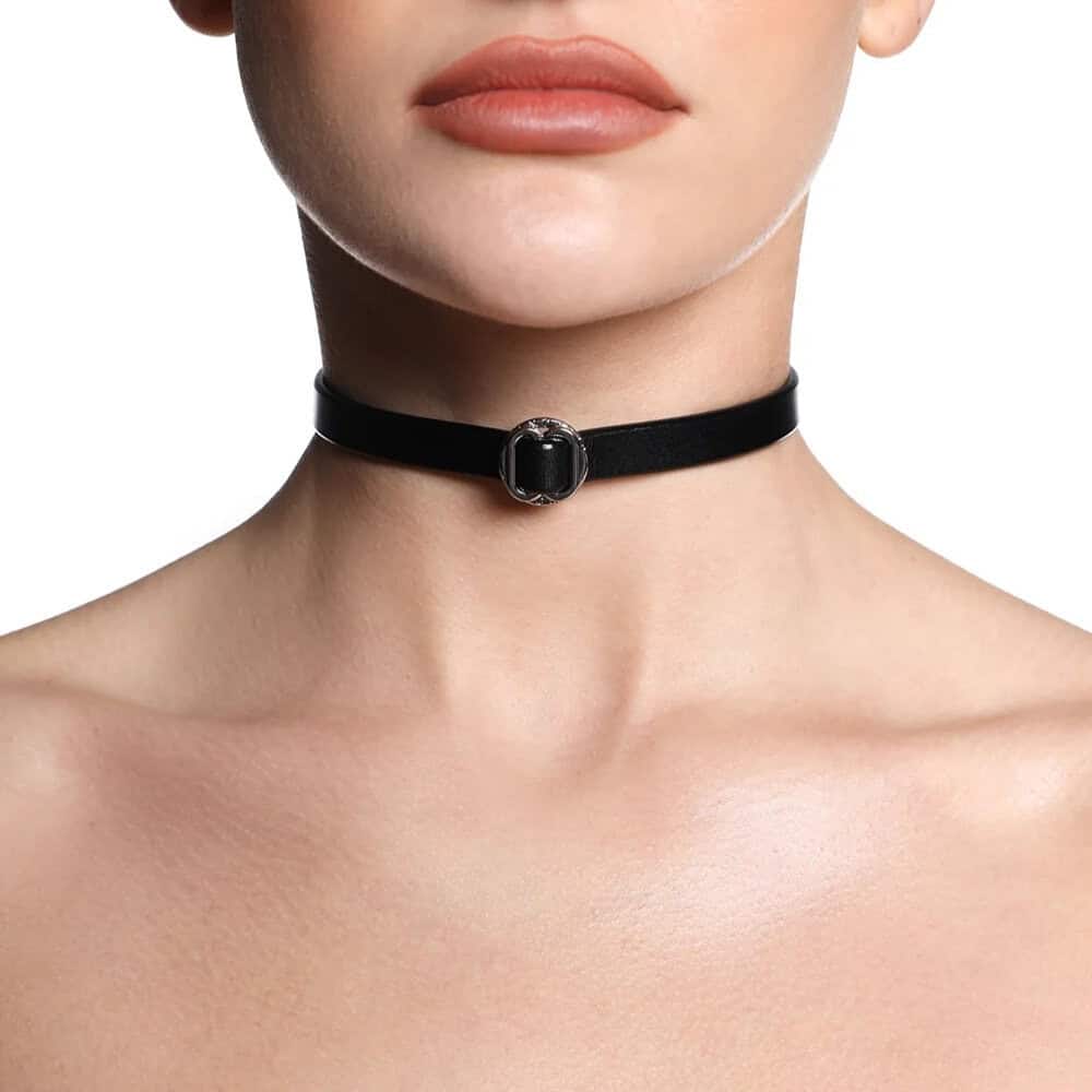 Collier ANOESES en cuir noir présenté à plat, bande fine avec anneau métallique central et fermeture réglable à boutons-pression, esthétique fétiche haut de gamme Brigade Mondaine Paris.