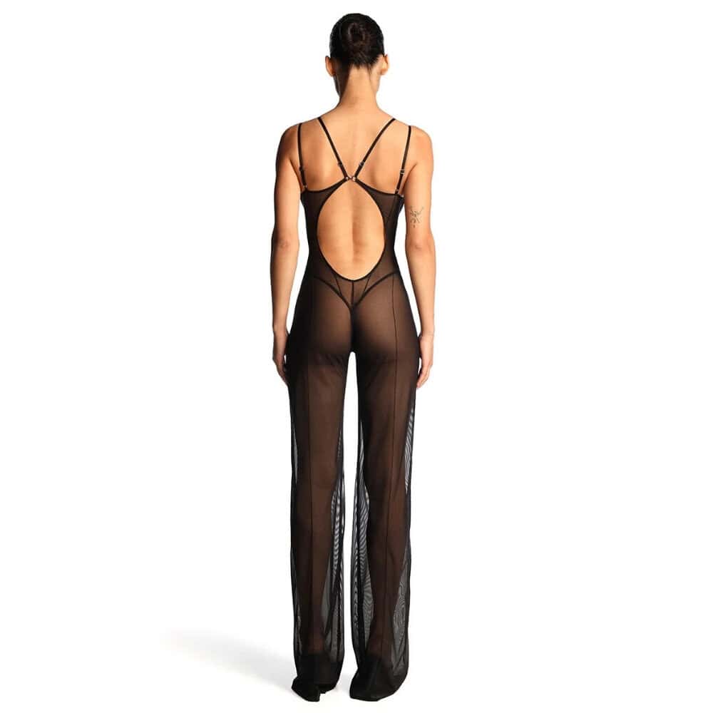 Catsuit ANOESES en mesh noir porté par un modèle féminin debout, coupe près du corps avec bretelles fines, lignes graphiques verticales et jambes longues transparentes, esthétique fétiche haut de gamme Brigade Mondaine Paris.