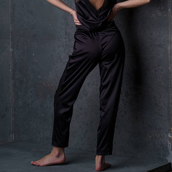 Le pantalon satin Nuit à Broadway porté par une femme, avec une ceinture froncée pour un confort optimal. Ses poches plaquées et ses bandes latérales lui donnent un look moderne et raffiné, idéal pour un ensemble homewear sexy.