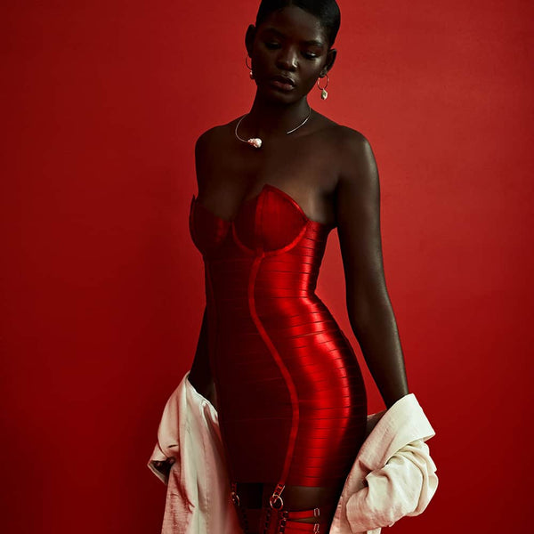 Robe Angela rouge de la marque Bordelle. Ce produit est composé de plus de cent cinquante élastiques en satin et de fermoir, réglages, porte jarretelles et une fermeture plaqués en or 24 carats. La robe est confectionné d’une accumulation d’élastiques qui moule le corps et d’elastiques qui imitent la forme d’un harnais. Pour le derrière, un zip est présent tout le long de la robe avec des anneaux de part et d’autre de la fermeture pour un effet corseté.