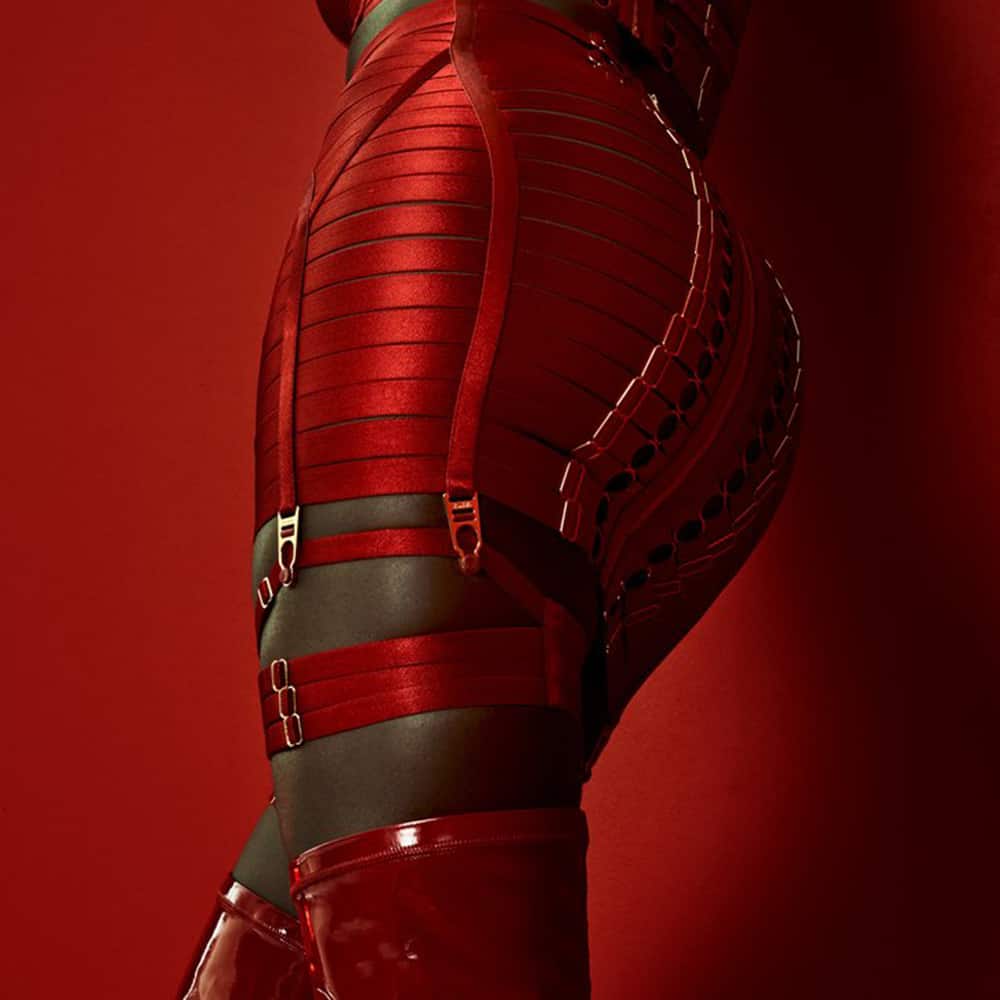 Jarretières WEBBED rouge de la marque Bordelle Signature . Elles sont composées de 4 fines bandes satinées. Chacune possède 4 détails en plaqué or. 2 pour les régler et 2 anneaux en guise de décoration. Elles sont traversées par une bande rouge en leur centre avec un anneau plaqué or au bout. 
