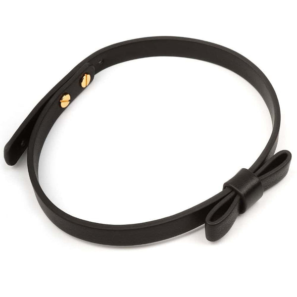 Set BDSM en cuir noir composé de liens ajustables avec anneaux dorés, d’un bandeau en tissu satiné et d’une plume noire montée sur manche doré, présenté sur fond blanc dans une esthétique épurée.