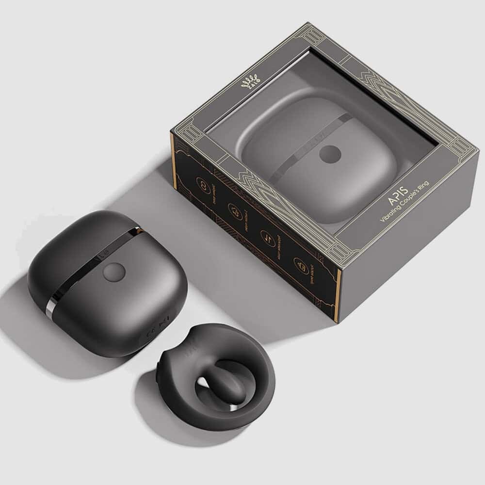 Cockring connecté APIS présenté avec son étui de recharge, câble USB et carte de garantie, disposés sur fond clair dans une mise en scène minimaliste et élégante.