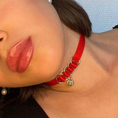 Collier BM inclut dans le pack cadeau Brigade Mondaine. Le produit est un choker simple avec un tour de cou en élastique rouge et un pendentif doré embossé du logo Brigade Mondaine. Ce bijoux est attaché au collier par quatre anneaux soutenus par l’entrelacement de l’élastique. L’ensemble du produit est réglable.