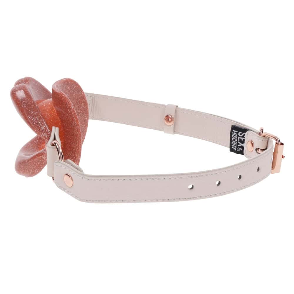 Gag ouvert au design en forme de lèvres avec sangle claire et finitions métalliques, présenté par Brigade Mondaine Paris sur fond clair.