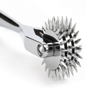 Roulette de Wartenberg en acier inoxydable brillant avec roulettes dentelées, design médical revisité, présentée par Brigade Mondaine Paris sur fond clair.