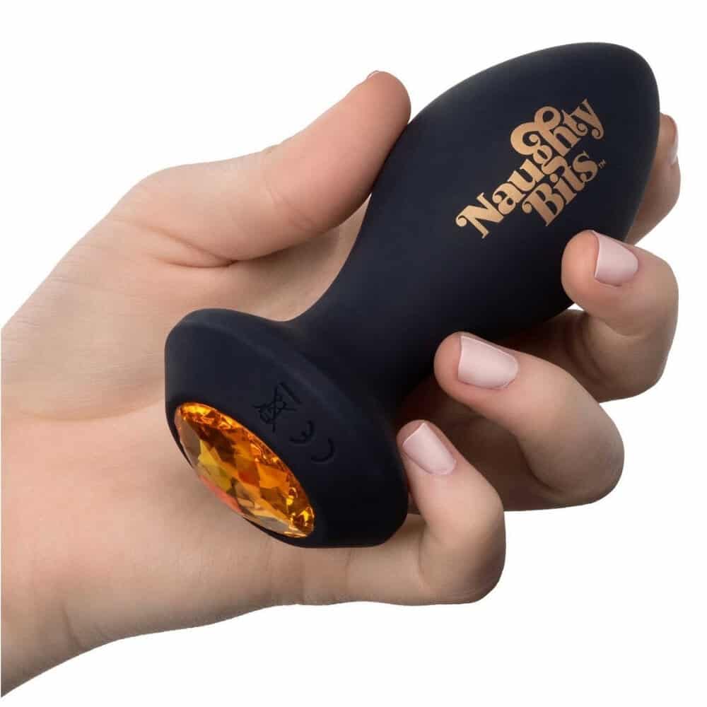 Plug anal noir en silicone avec base ornée d’un bijou facetté ambré, tenu en main, proposé par Brigade Mondaine Paris.