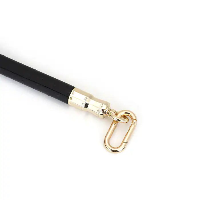 Barre d’écartement en cuir noir embossé peau d’autruche avec clips à dégagement rapide et finitions dorées. Accessoire BDSM de contrôle élégant.