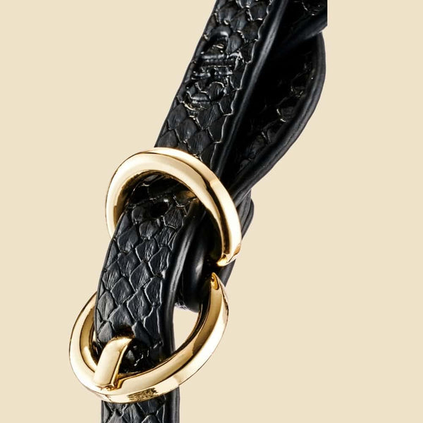 Bâillon boule BDSM composé d’une boule noire mate et de sangles en cuir noir texturé avec rivets et bouclerie dorée, présenté sur fond sombre dans une mise en scène élégante.