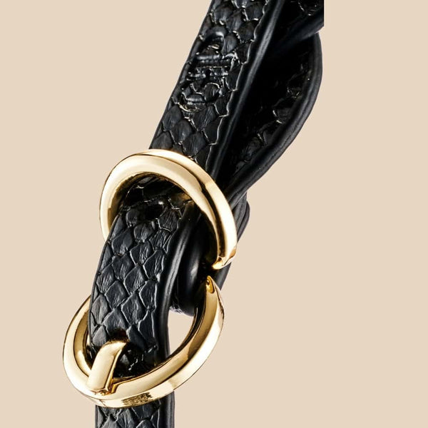 Masque BDSM en cuir noir texturé à la forme enveloppante, avec attaches réglables et bouclerie dorée, présenté sur fond noir dans une mise en scène élégante et minimaliste.