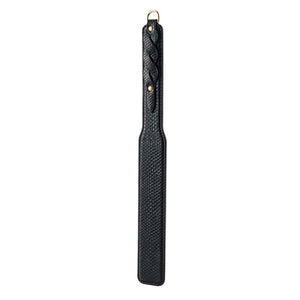 Modèle portant un body noir transparent et tenant un paddle BDSM en cuir noir à finition texturée, photographiée sur fond blanc dans une mise en scène épurée et élégante.