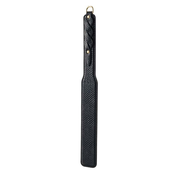Modèle portant un body noir transparent et tenant un paddle BDSM en cuir noir à finition texturée, photographiée sur fond blanc dans une mise en scène épurée et élégante.