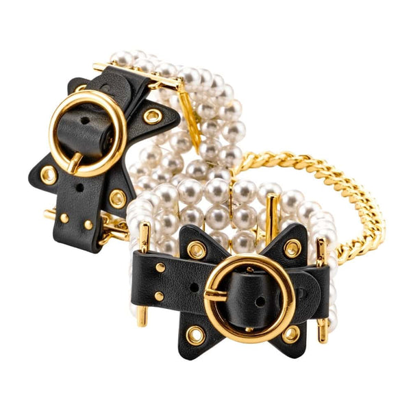 Entraves de chevilles en cuir noir ornées de perles et reliées par une chaîne dorée, portées sur modèle, proposées par Brigade Mondaine Paris.