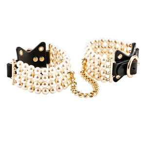 Entraves de chevilles en cuir noir ornées de perles et reliées par une chaîne dorée, portées sur modèle, proposées par Brigade Mondaine Paris.
