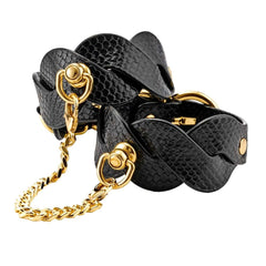 Chevilles d’un modèle portant des menottes BDSM noires texturées reliées par une chaîne dorée, accessoire de contrainte sélectionné par Brigade Mondaine Paris.