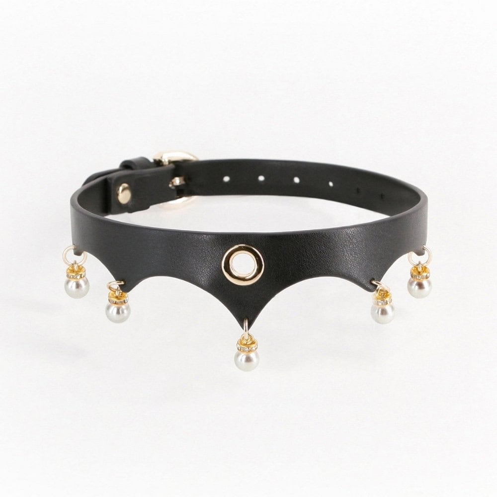 Gros plan d’un collier BDSM en cuir noir porté au cou, orné d’anneaux dorés et de perles blanches, sur fond sombre, dans une esthétique élégante et minimaliste.