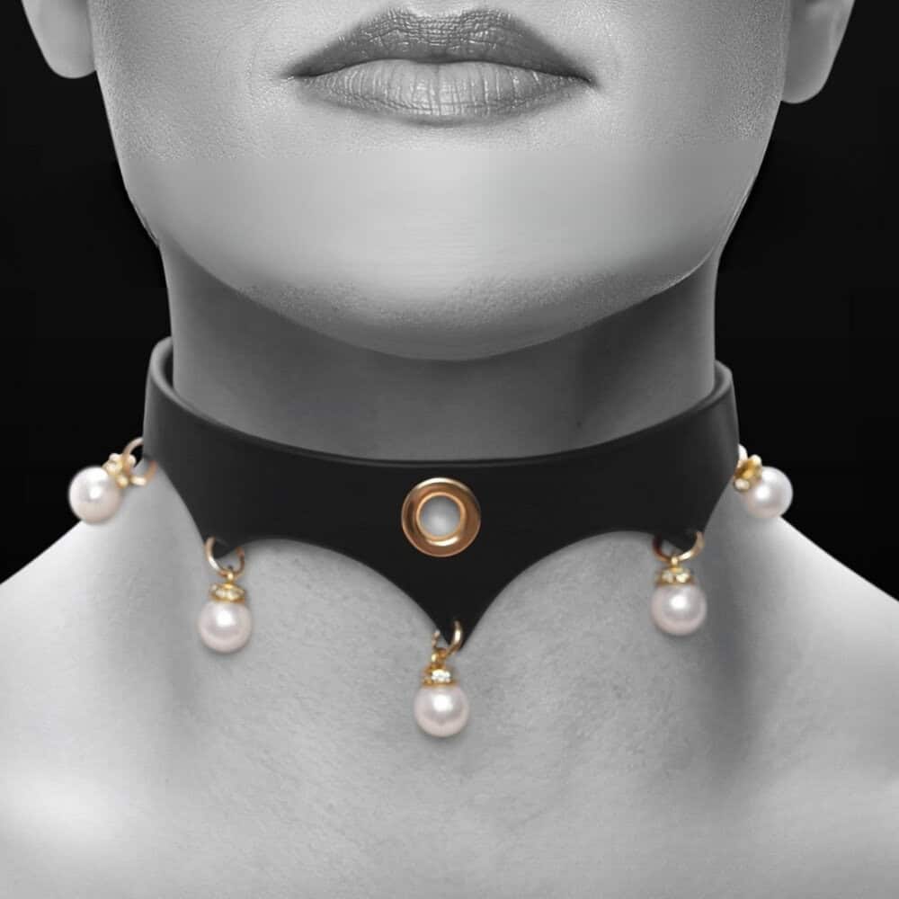 Gros plan d’un collier BDSM en cuir noir porté au cou, orné d’anneaux dorés et de perles blanches, sur fond sombre, dans une esthétique élégante et minimaliste.