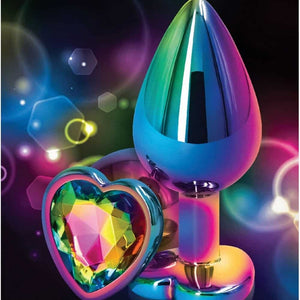 Plug anal en cristal multicolore avec base décorative en forme de cœur facetté, présenté sur fond sombre avec effets lumineux et reflets irisés.