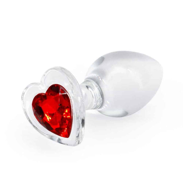 Plug anal en cristal transparent posé sur fond noir, avec une base décorative en forme de cœur rouge facetté, à l’esthétique élégante et raffinée.