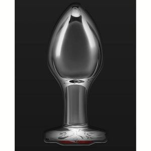 Plug anal en cristal transparent posé sur fond noir, avec une base décorative en forme de cœur rouge facetté, à l’esthétique élégante et raffinée.