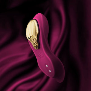 Vibromasseur portable de couleur prune avec détails dorés, design ergonomique et commandes intégrées, présenté sur fond blanc, sélection Brigade Mondaine Paris.