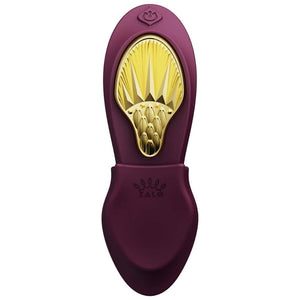 Vibromasseur portable de couleur prune avec détails dorés, design ergonomique et commandes intégrées, présenté sur fond blanc, sélection Brigade Mondaine Paris.