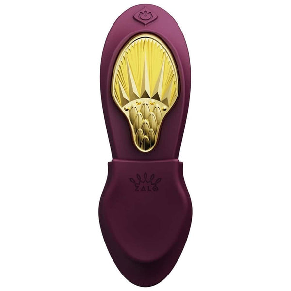 Vibromasseur portable de couleur prune avec détails dorés, design ergonomique et commandes intégrées, présenté sur fond blanc, sélection Brigade Mondaine Paris.