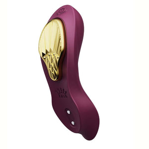 Vibromasseur portable de couleur prune avec détails dorés, design ergonomique et commandes intégrées, présenté sur fond blanc, sélection Brigade Mondaine Paris.