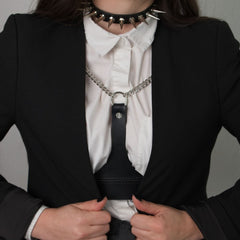 Femme portant le choker 86137 avec chemise blanche, blazer noir et harnais en cuir noir orné de chaînes argentées. Le choker est décoré de spikes métalliques et se ferme à l’arrière avec une boucle réglable.