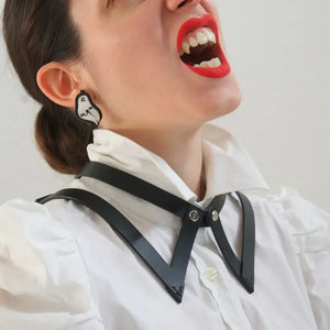 Vue rapprochée du choker 86647 en cuir noir porté sur une chemise blanche avec col, mettant en avant le design inspiré du col de chemise. La femme porte du rouge à lèvres rouge et affiche des dents légèrement vampiriques, ajoutant une touche audacieuse à son look.
