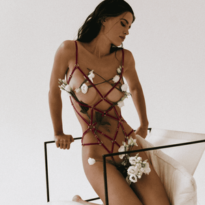 Photographie d'un corps de femme portant un playsuit fuchsia avec des fleurs blanches dispersées sur son corps avec le harnais.