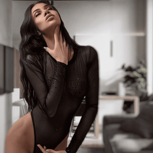 femme qui se caresse le cou, elle porte un bodysuit noir transparent devant un fond flou