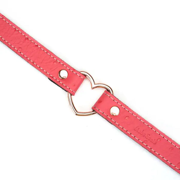 Choker Cœur en cuir rose embossé peau d’autruche avec cœur central en métal or rose. Boucle métallique robuste. Accessoire fétichiste séduisant et affirmatif. Ajustable pour un confort parfait.