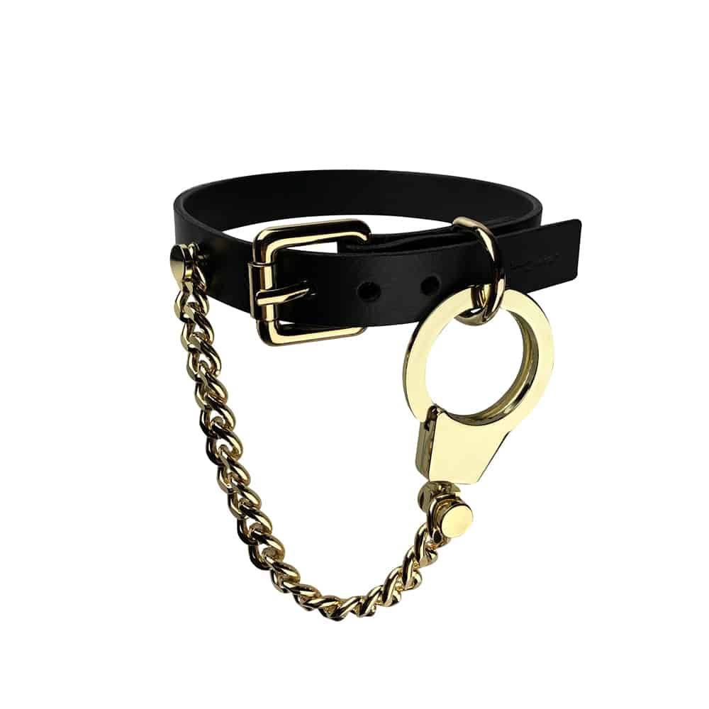 Collier Menottes chaines et cuir de la marque ELF ZHOU LONDON. le collier est attaché autour du cou du mannequin. La partie en cuir du collier est attachée et la chaine en or rattachée au collier par la menotte en or pend.