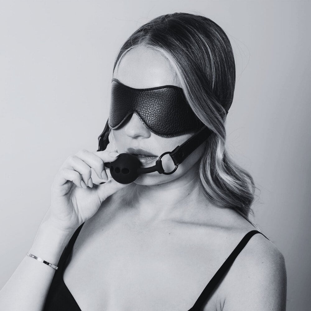 Bandeau en cuir noir avec sangle élastique et gag en silicone noir intégré, accessoire BDSM proposé par Brigade Mondaine Paris.