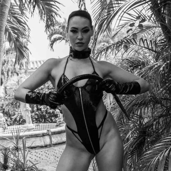 Photo Femme portant Body Cuir Noir Serpens, un Collier Bondage en Cuir de Vachette Noir et Anneau Métal et une Queue d'Impact Noire en Cuir
