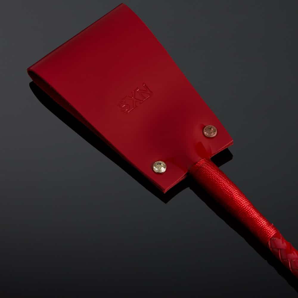 Cravache en vernis rouge HOUSE OF SXN avec manche rigide et extrémité plate, accessoire BDSM haut de gamme proposé par Brigade Mondaine Paris.