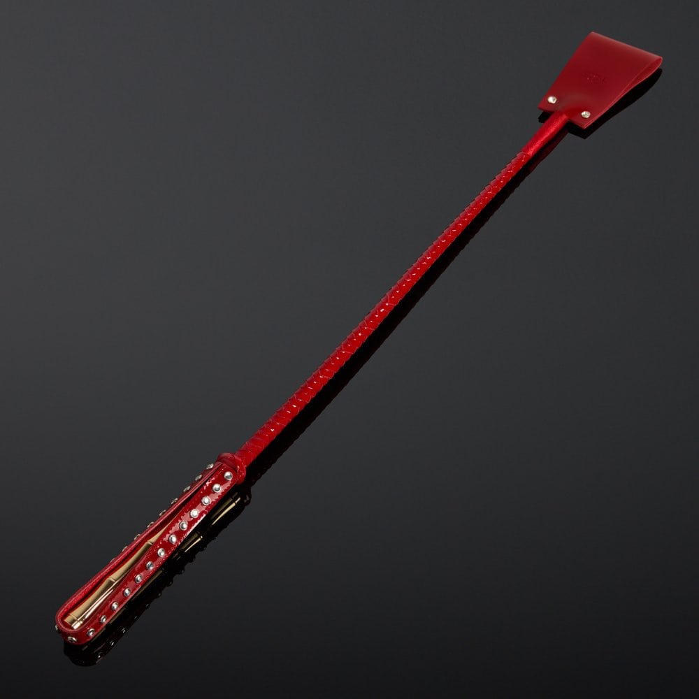 Cravache en vernis rouge HOUSE OF SXN avec manche rigide et extrémité plate, accessoire BDSM haut de gamme proposé par Brigade Mondaine Paris.