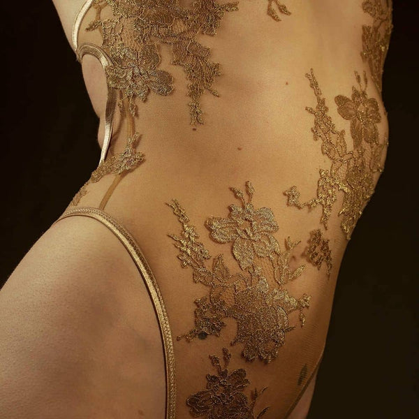 Le body licou AMMALIE sublime la silhouette avec son effet seconde peau et son éclat doré subtil. Confectionné à la main en maille illusion ultra-transparente, il épouse le corps avec finesse. Son appliqué en dentelle Leavers française en or rosé, découpé et cousu à la main, ajoute une touche précieuse. Les bretelles dorées réglables et les accessoires plaqués or 24 carats assurent un ajustement parfait. Pour un confort optimal, l’intérieur est doublé en coton de bambou biologique.