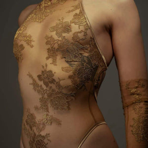Le body licou AMMALIE sublime la silhouette avec son effet seconde peau et son éclat doré subtil. Confectionné à la main en maille illusion ultra-transparente, il épouse le corps avec finesse. Son appliqué en dentelle Leavers française en or rosé, découpé et cousu à la main, ajoute une touche précieuse. Les bretelles dorées réglables et les accessoires plaqués or 24 carats assurent un ajustement parfait. Pour un confort optimal, l’intérieur est doublé en coton de bambou biologique.