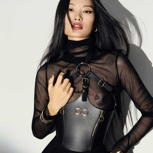 Corset Bondage HOSTIA IINFYNII noir avec sangles et anneaux métalliques porté sur un top en mesh, pièce structurée proposée par Brigade Mondaine Paris
